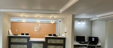 Un espace d’accueil d’hôtel au design moderne, comprenant un comptoir d’accueil, un poste informatique et un lustre.