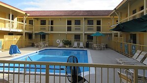 Um hotel com área de piscina, mobiliário ao ar livre e um edifício de dois andares com varandas.