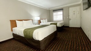 Quarto de hotel com duas camas, uma janela, uma porta e uma televisão de tela plana fixada na parede.
