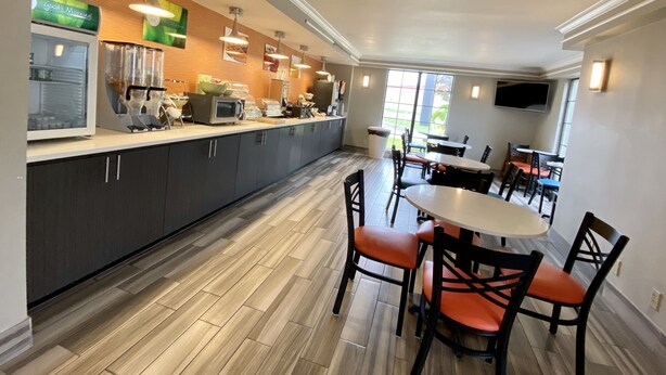 Um restaurante moderno com um balcão extenso, diversas áreas de estar e uma grande janela que oferece luz natural.