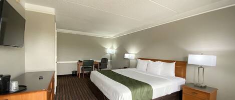 A hotel room with a bed, desk, chair, TV, and lamps.