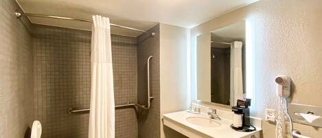 A bathroom with a shower, a toilet, a sink, a mirror, and a hair dryer.
