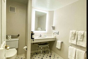 A small bathroom with a toilet, sink, and a mirror. There is a step stool under the sink.