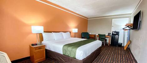 Quarto de hotel com uma cama grande, duas mesas de cabeceira com luminárias, uma escrivaninha com cadeira, televisão na parede e piso coberto por carpete.