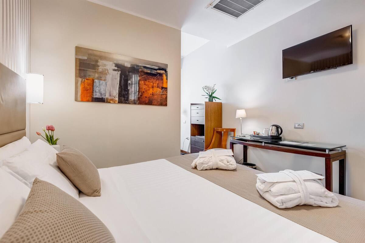 A hotel room with a bed, a desk, a flat-screen TV, and a painting on the wall.