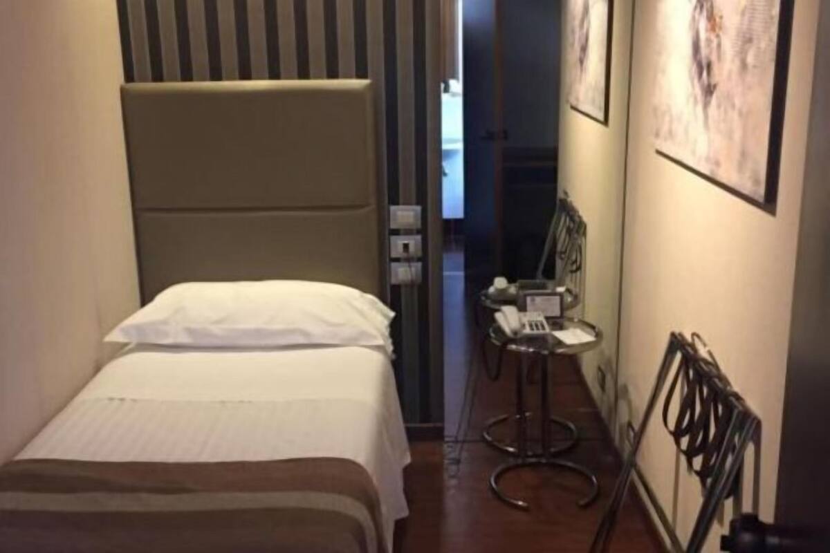 A hotel room with a bed, a small table with a telephone, and a chair.