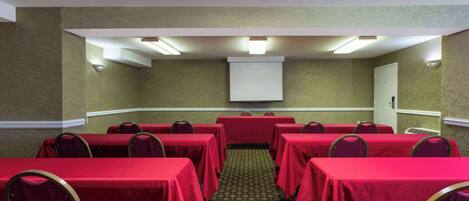 A conference room with tables covered in red tablecloths, arranged in a U-shape around a central whiteboard.