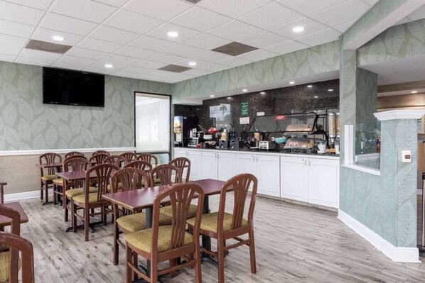 A restaurant with wooden tables and chairs, a kitchen area, and a flat-screen TV mounted on the wall.