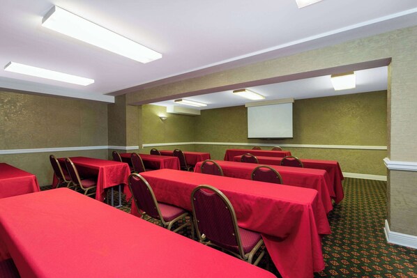 Une salle de conférence avec des tables recouvertes de nappes rouges, disposées en rangées et entourées de chaises.