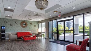 En lobby med en rød sofa, en beige sofa, en rød lænestol og trægulv. Der er en lysekrone, et spejl og et skilt med teksten "EXIT".