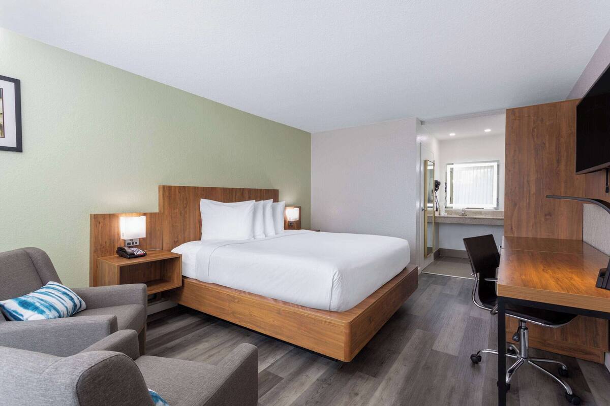 A hotel room with a wooden bed, a desk, a chair, a nightstand, and a television.