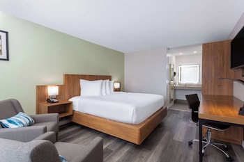 A hotel lobby with a coffee station, a seating area with a red couch, and a decorative wall with a mirror and a chandelier. at Ramada by Wyndham Altamonte Springs Near I-4
