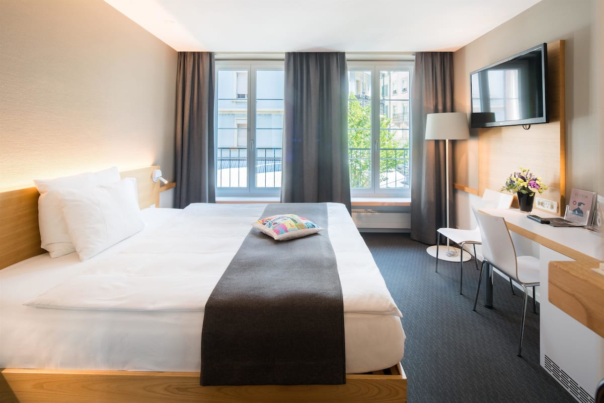 A hotel room with a bed, a desk, a chair, a TV, and a window with curtains.