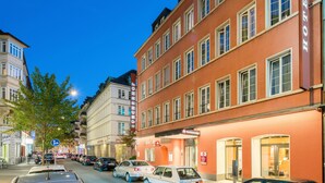 Une vue de rue avec une rangée de voitures garées, un bâtiment portant une enseigne indiquant « Best Western PLUS », et un arbre au premier plan.