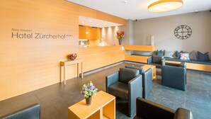 Un espace d’accueil d’hôtel avec un comptoir de réception en bois, une horloge au mur et des sièges.
