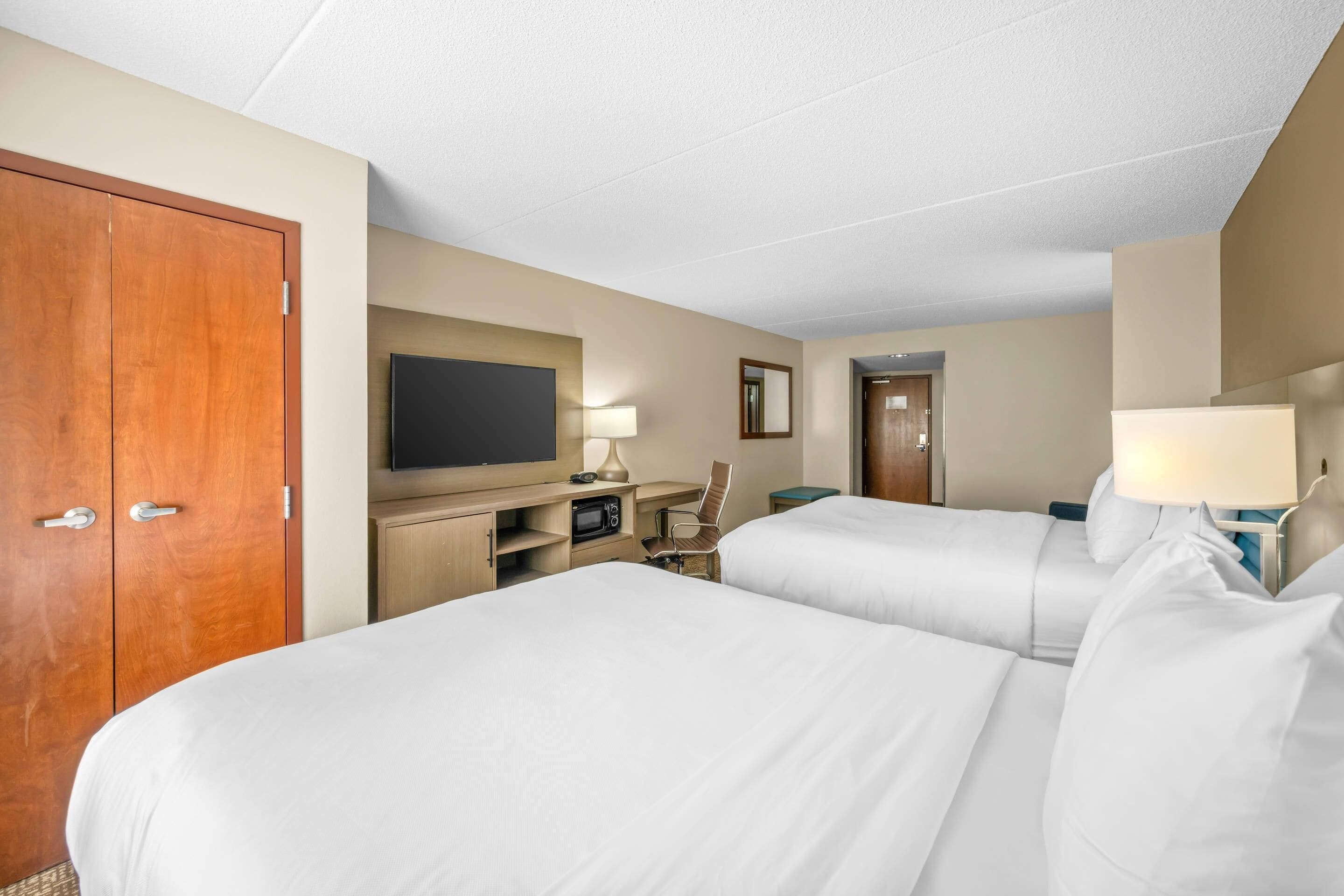 A hotel room with two beds, a desk, a television, a chair, and a wardrobe.