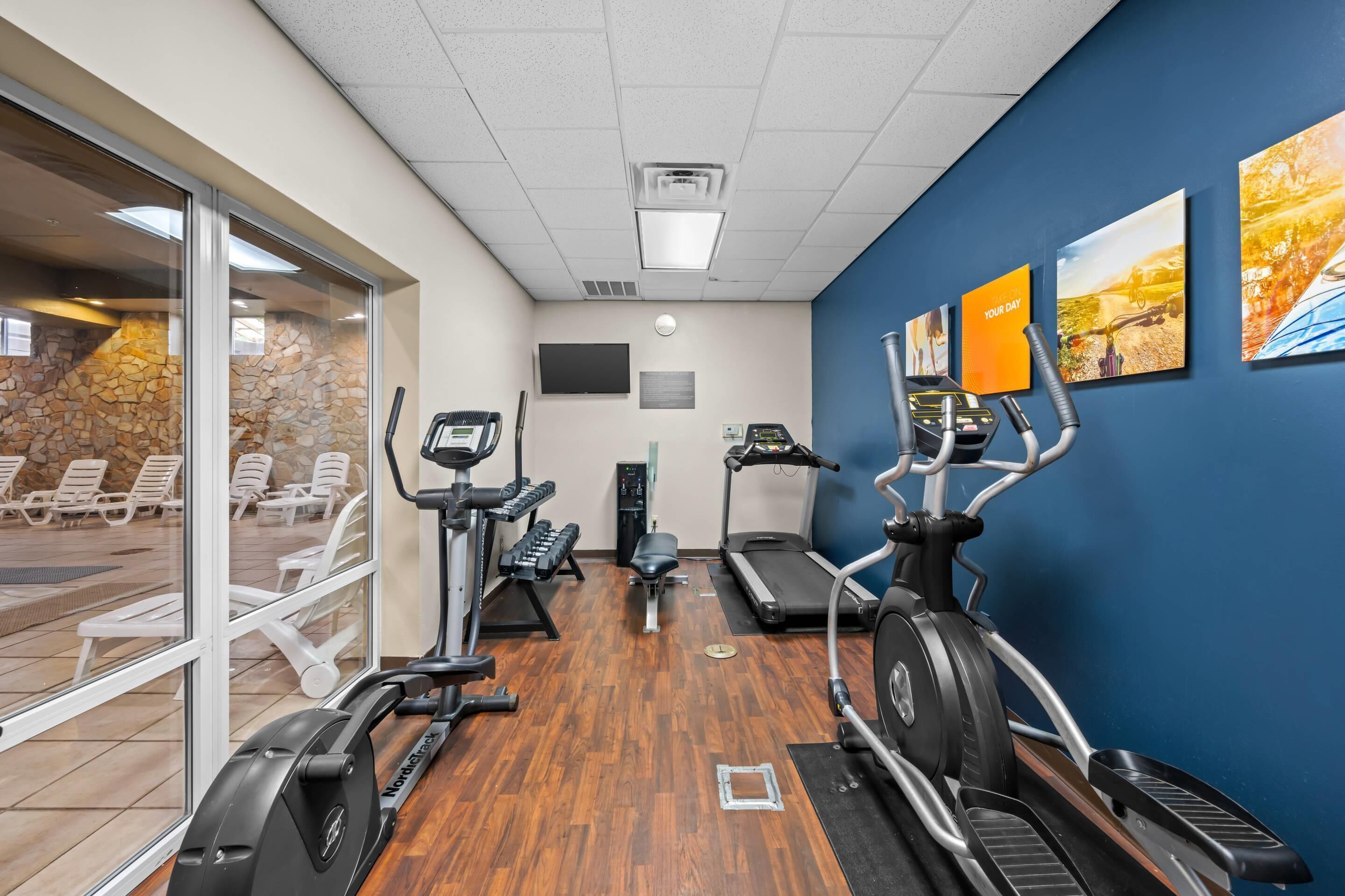 Une salle de sport équipée de matériel d’exercice, d’un distributeur d’eau et offrant une vue sur un espace de détente extérieur.