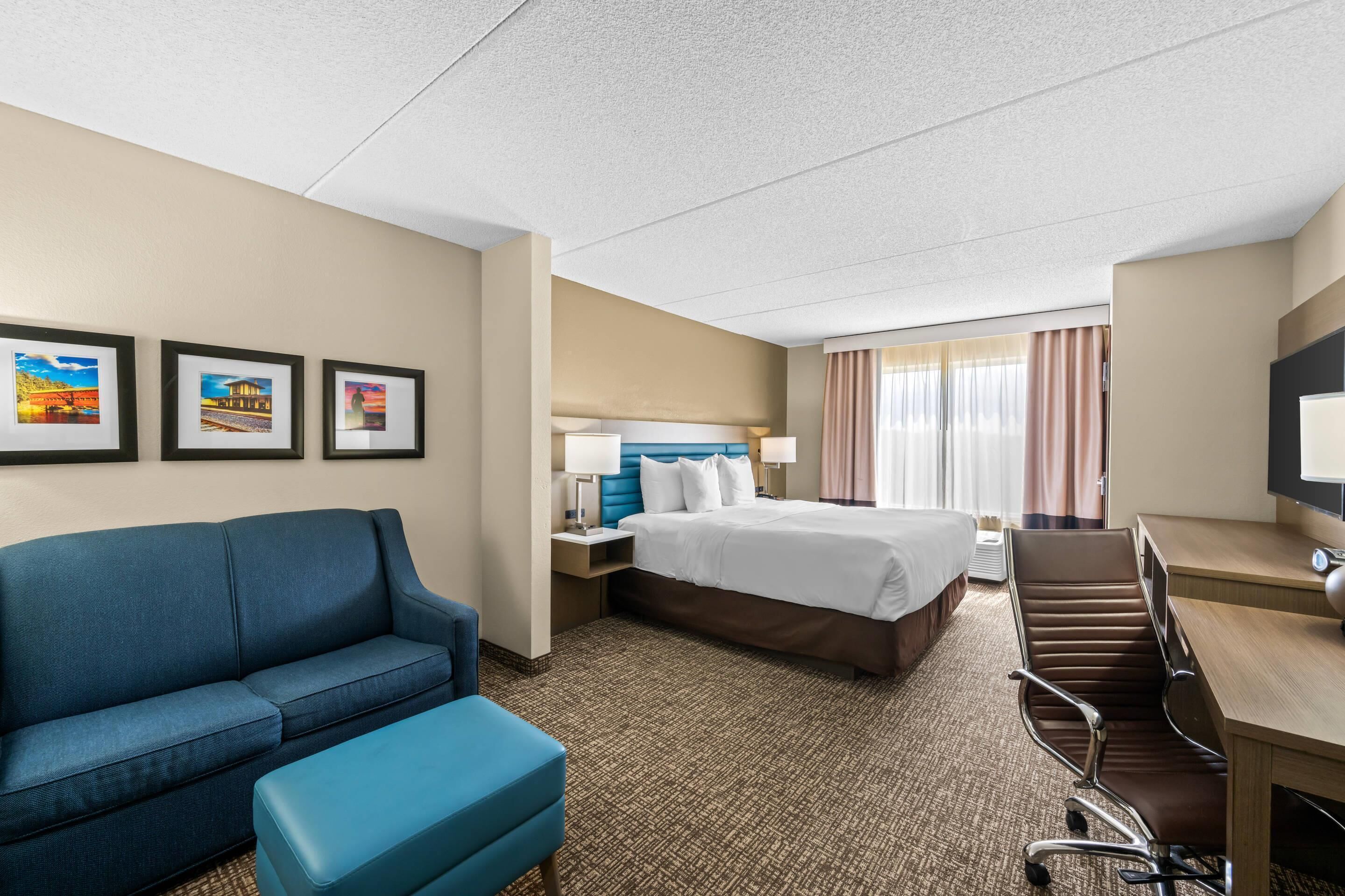 A hotel room with a bed, a desk, a chair, a sofa, and a television.