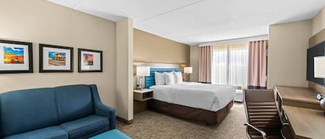 A hotel room with a bed, a desk, a chair, a sofa, and a television.