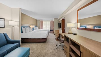 A hotel room with a large bed, a desk with a chair, a sofa, and a TV.