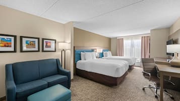 A hotel room with a sofa, two beds, a desk, and a chair.