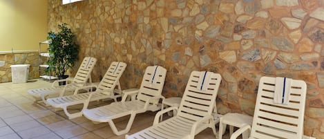 A row of white sun loungers against a stone wall with a window above.
