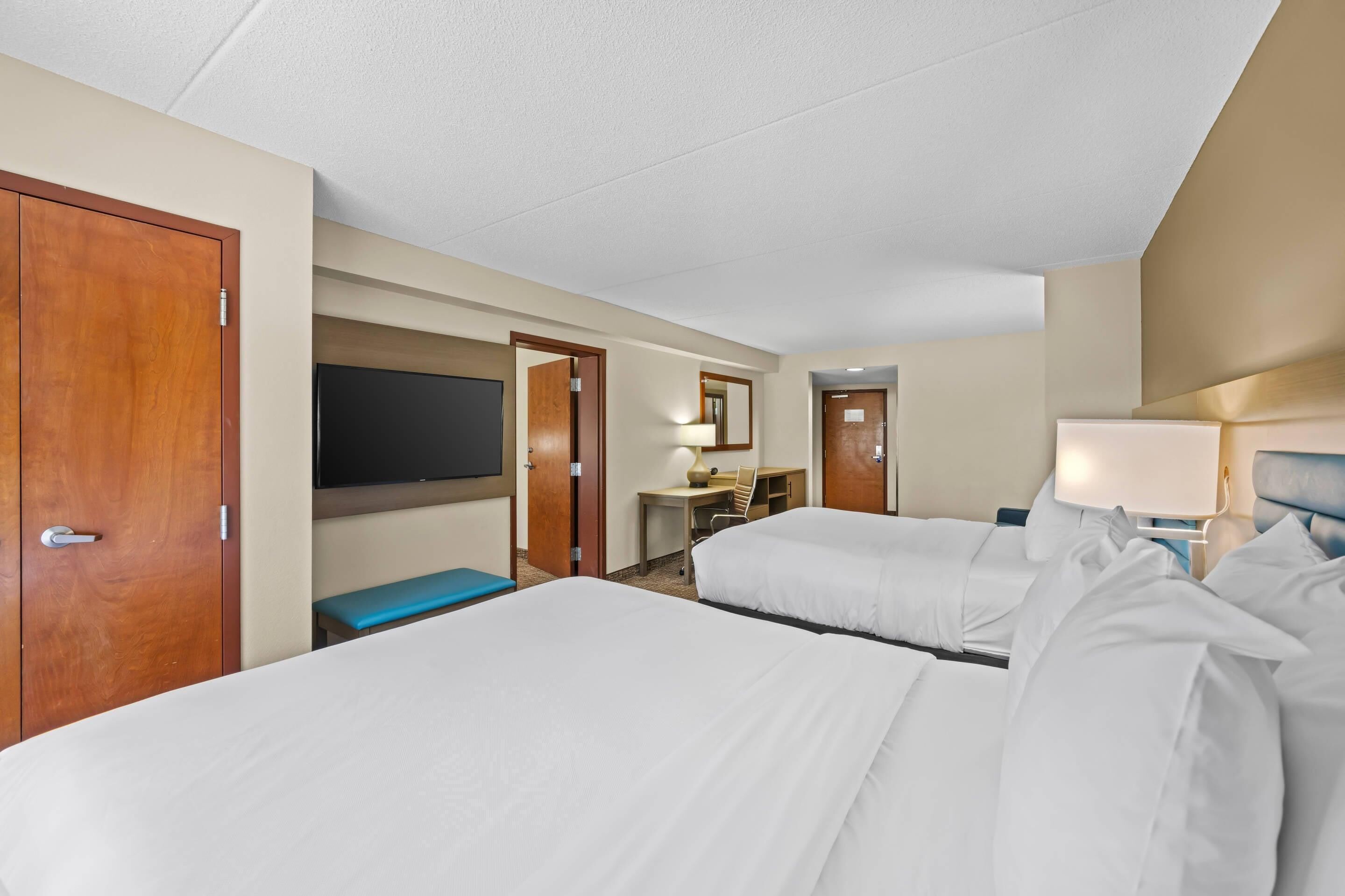 Een hotelkamer met twee bedden, een bureau, een stoel, een televisie en een deur.