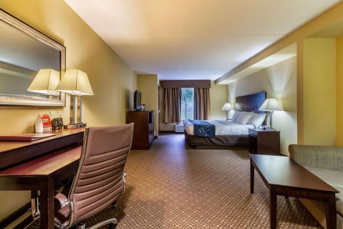 A hotel room with a bed, a desk with a chair, a TV, a lamp, and a window with curtains.