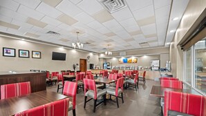 A spacious dining area with multiple tables and chairs, a counter with a cash register, and a wall-mounted television.