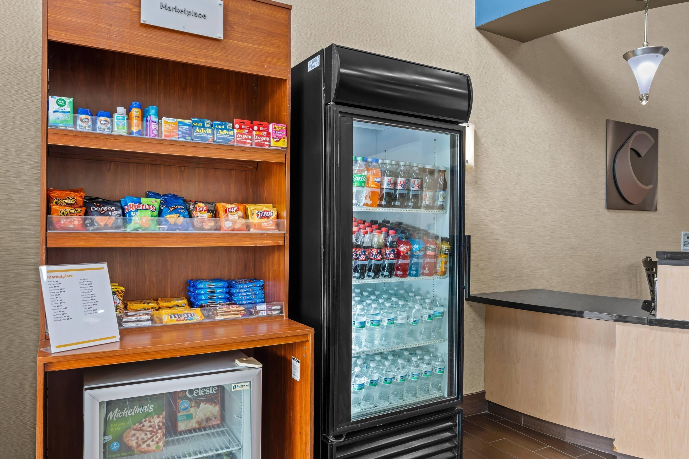Una estación de bebidas de autoservicio con un refrigerador para bebidas y estantes con snacks.