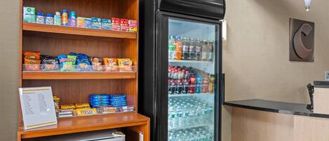 A self-service beverage station with a refrigerated drink cooler and snack shelves.