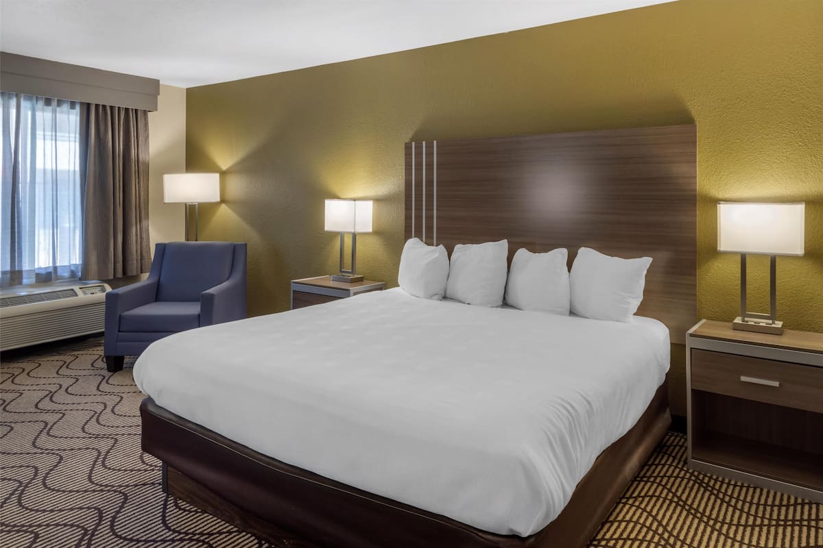 A hotel room with a large bed, two bedside tables with lamps, a chair, and a window with curtains.