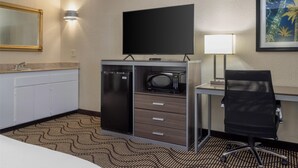 A hotel room with a kitchenette, a flat-screen TV, a desk with a chair, a lamp, and a framed picture on the wall. - Best Western Heritage Inn (Concord)