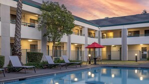 A hotel with a swimming pool, lounge chairs, and a red umbrella. - Best Western Heritage Inn (Concord)