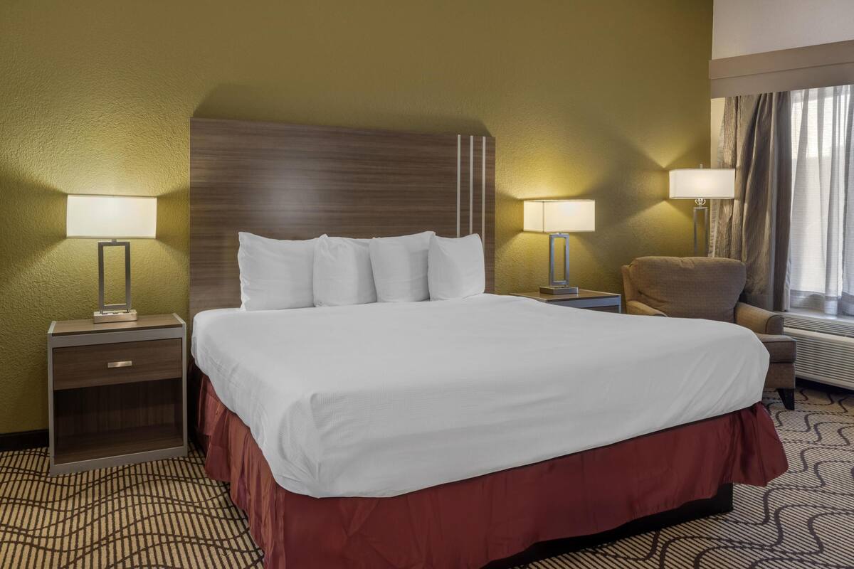 A hotel room with a large bed, two bedside tables with lamps, a chair, and a window with curtains.