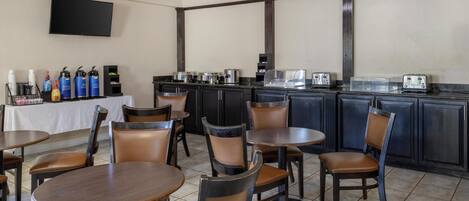 A restaurant with round tables and chairs, a bar area with a TV, and various kitchen appliances.