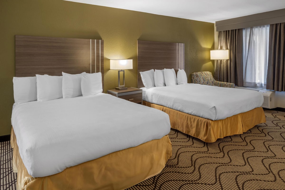 A hotel room with two beds, a nightstand, a chair, and a window with curtains.