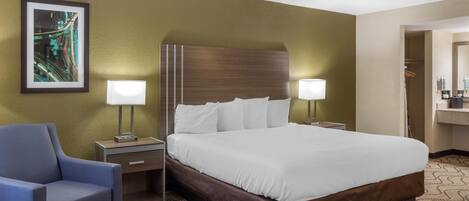 A hotel room with a large bed, two bedside tables with lamps, a chair, a framed picture on the wall, and a patterned carpet.