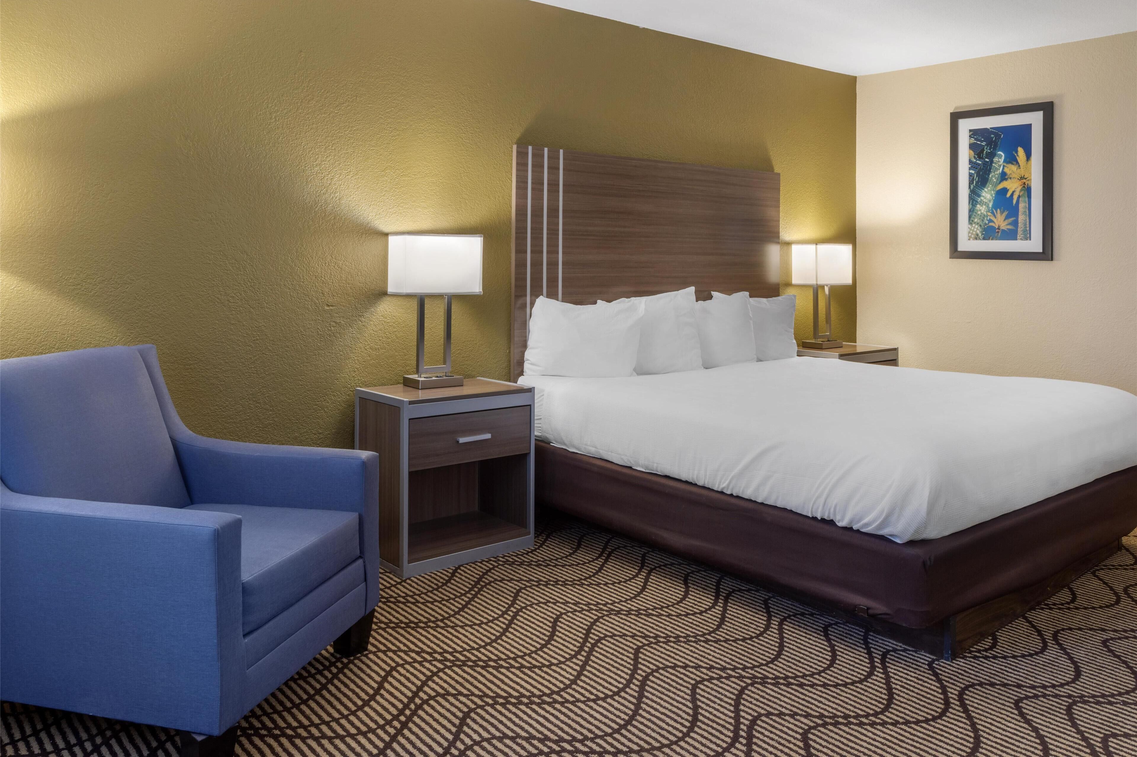 A hotel room with a bed, two bedside tables with lamps, a blue armchair, and a patterned carpet.