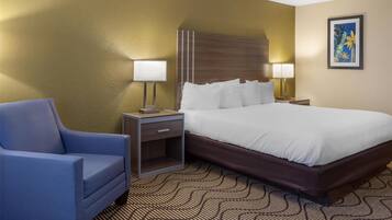 A hotel room with a bed, two bedside tables with lamps, a blue armchair, and a patterned carpet.