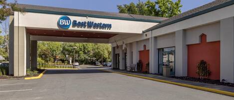 A Best Western hotel entrance with a covered walkway, parking lot, and greenery in the background.