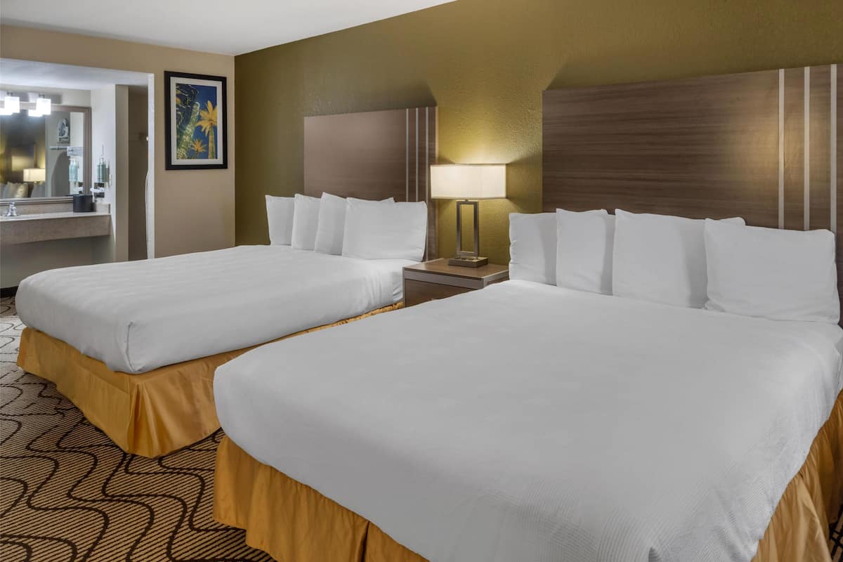 A hotel room with two beds, a large mirror, a painting, and a nightstand with a lamp.