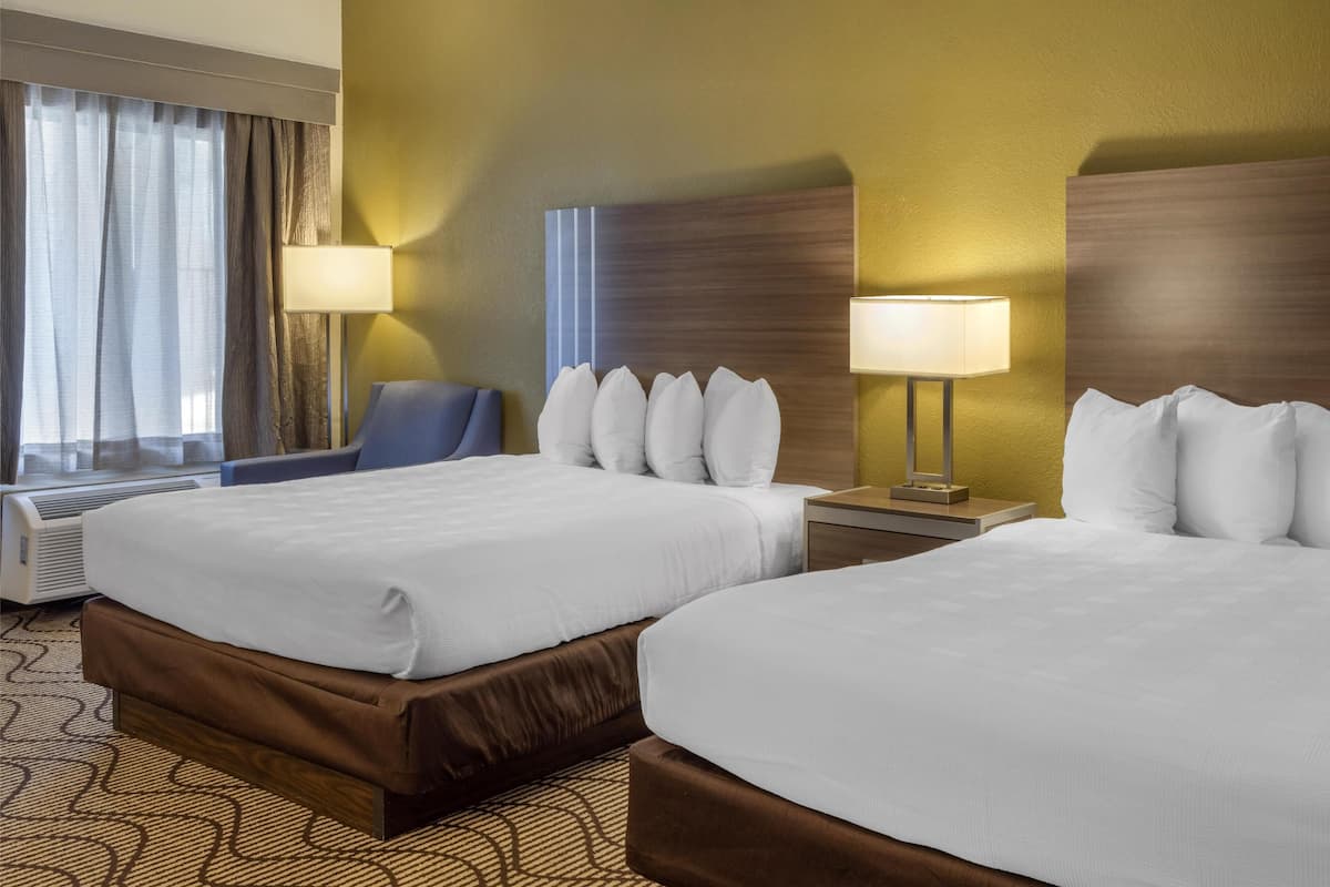 A hotel room with two beds, a desk, a chair, and a window with curtains.