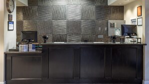 A reception desk with a patterned wall, a clock, and framed certificates. - Best Western Heritage Inn (Concord)