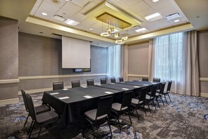 A conference room with a long table, chairs, a projector screen, and a large window with curtains. - Embassy Suites by Hilton Montgomery Hotel & Conference Ctr (Montgomery)