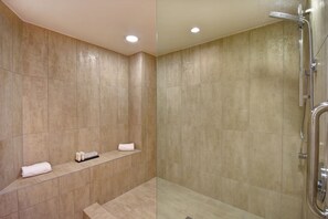 Un baño moderno con baldosas color beige, cabina de ducha de vidrio y un estante con artículos de aseo.