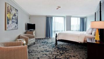 A hotel room with a bed, a television, a desk, a chair, and a large window with curtains.