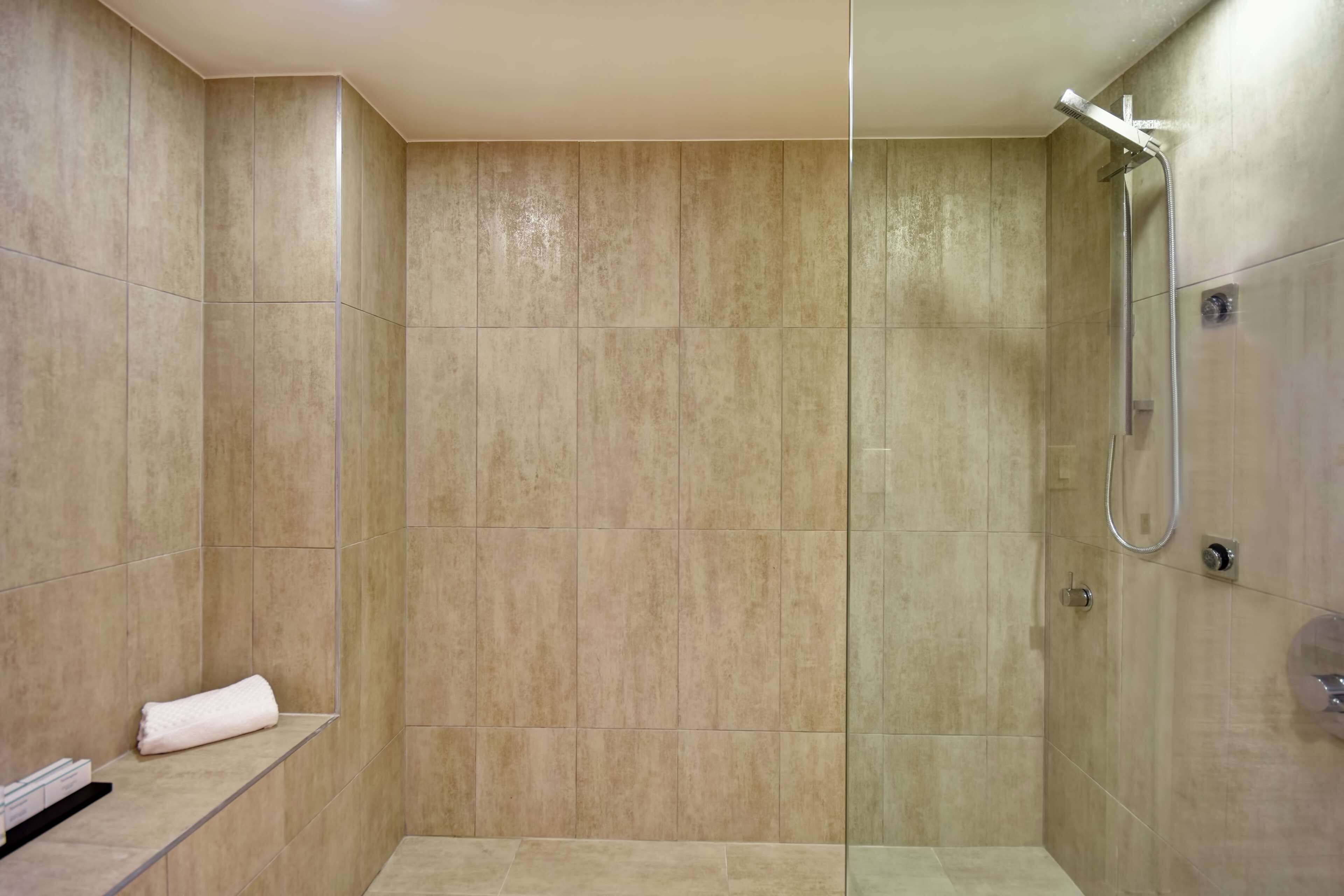 A modern shower with a glass partition, beige tiles, and a towel on a shelf.