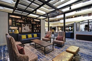 A spacious lobby with a high ceiling, a blue sofa with yellow cushions, and a patterned carpet. - Embassy Suites by Hilton Montgomery Hotel & Conference Ctr (Montgomery)