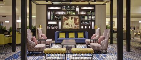 A lobby with a blue sofa, two armchairs, a coffee table, and a bookshelf with various items.